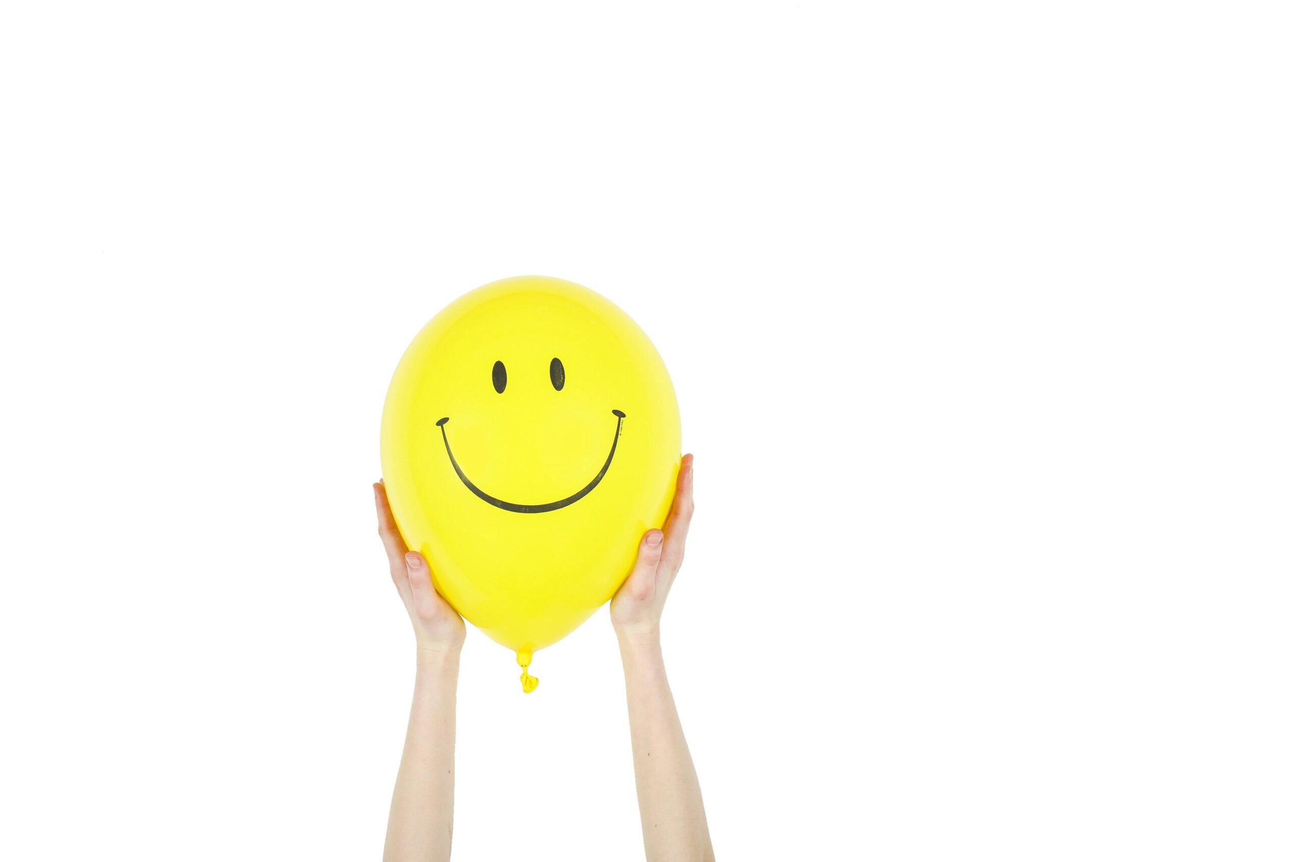 Cheerful yellow balloon with a smiley face held up by hands against a white background.